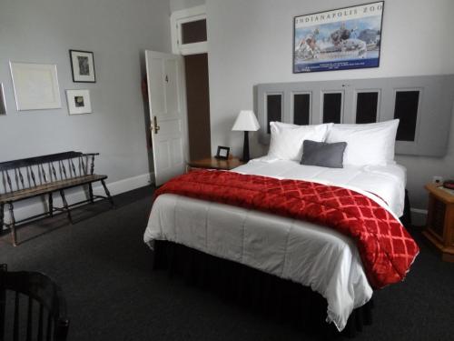 A cozy hotel room featuring a bed with a red throw, a wooden bench, and framed artwork on the walls.