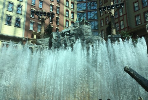 Indoor waterfall cascading over rocks, surrounded by a glass atrium and colorful buildings.