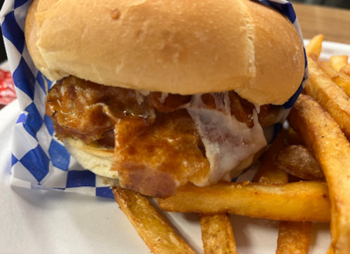 A close-up of a chicken sandwich with crispy chicken and melted cheese, served with golden French fries on the side.
