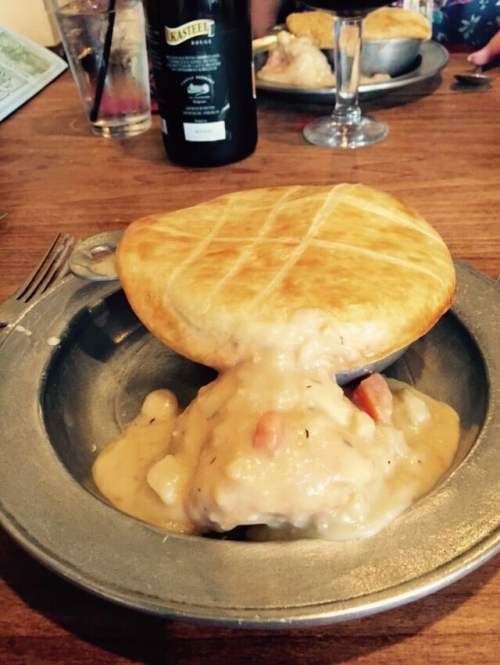 A golden-brown pie crust sits atop creamy chicken and vegetable filling in a metal dish on a wooden table.