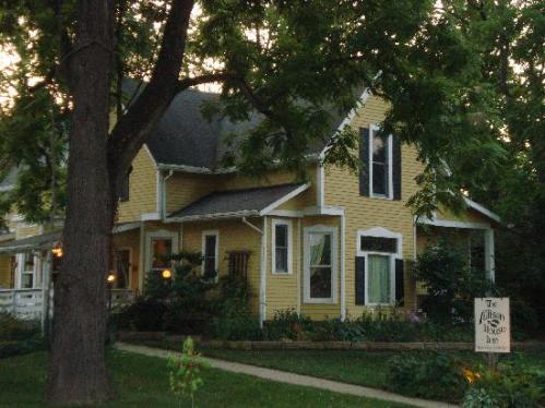A charming yellow house with a porch, surrounded by trees and a garden, featuring a sign for "The Abbey House Inn."