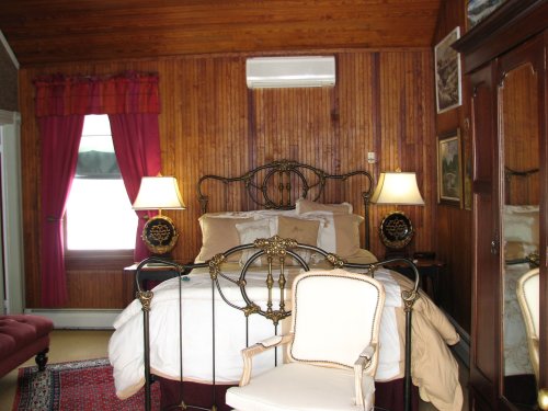 Cozy bedroom with wooden walls, a wrought iron bed, two lamps, and a vintage chair, creating a warm atmosphere.