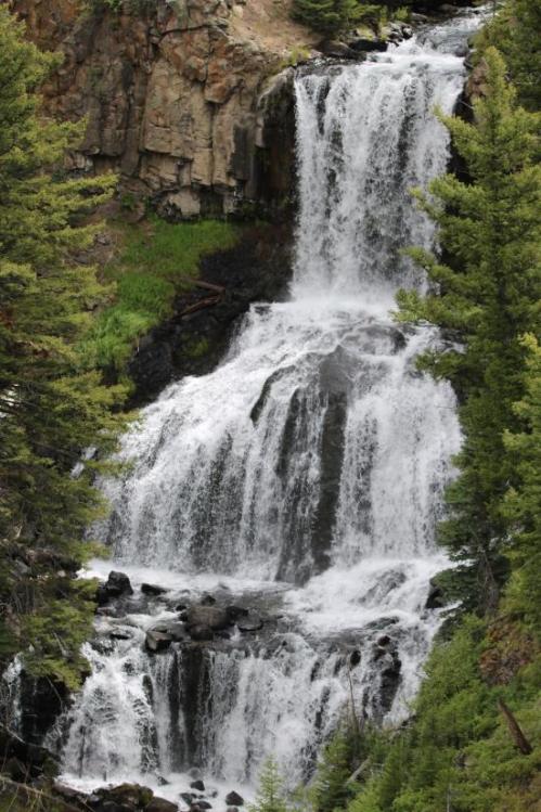 A cascading waterfall surrounded by lush green trees and rocky cliffs. Water flows over multiple tiers into a serene pool.