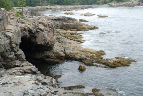 Rocky coastline with water, small islands, and lush greenery in the background on a cloudy day.