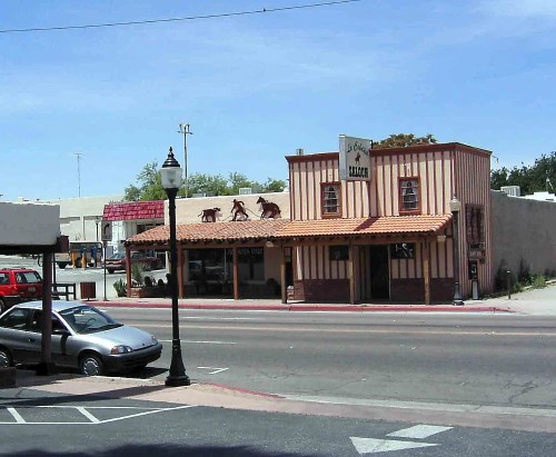A rustic building with a red and white striped facade, featuring a sign and decorative figures on the roof, set on a street.