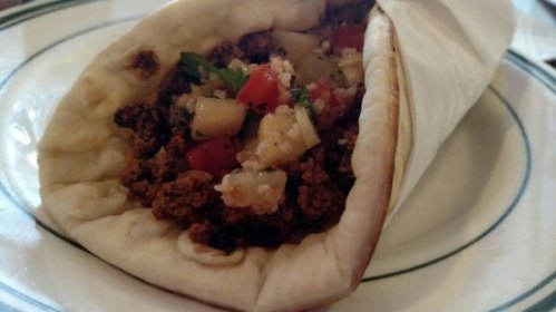 A close-up of a wrapped burrito filled with seasoned meat, diced tomatoes, and herbs on a plate.