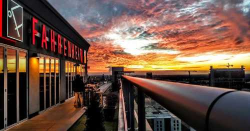 Sunset view from a rooftop with the word "FAHRENHEIT" illuminated, featuring vibrant clouds and a city skyline.