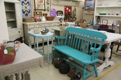 A cozy vintage shop displaying various furniture pieces, including a turquoise bench and tables, with decorative items.
