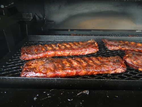 Four racks of smoked ribs on a grill, glistening with a rich, dark glaze.