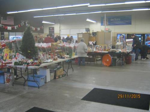 A bustling indoor market with tables displaying holiday items and decorations, and shoppers browsing around.