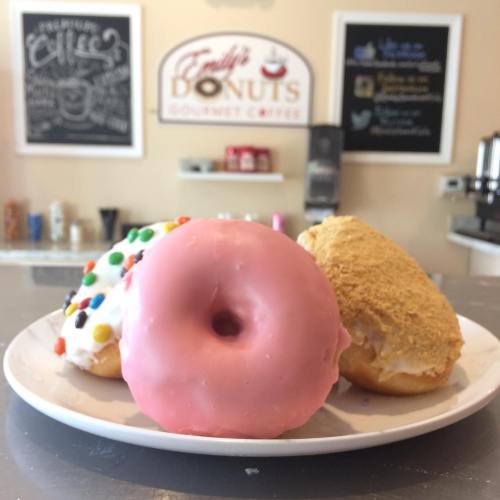 A plate of three colorful donuts: one pink frosted, one with sprinkles, and one with a crumb topping.