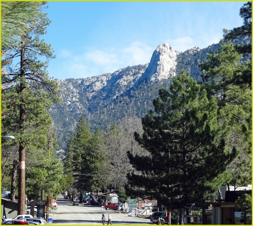 A scenic view of a mountain peak surrounded by tall trees and a quiet street below.