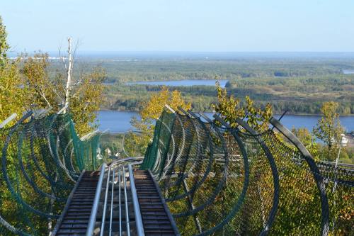 A scenic view from a hilltop roller coaster track overlooking a river and lush green landscape.