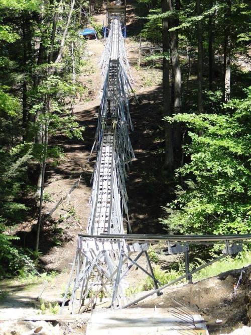A metal track runs through a forest, leading downhill among trees and greenery.
