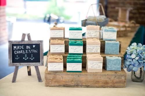 A display of handmade soaps in various colors on a wooden stand, with a sign reading "Made in Charleston."