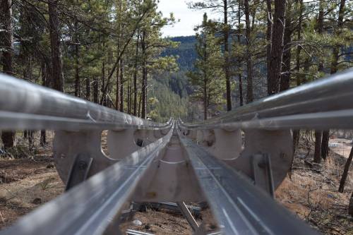 View down a metal track through a forest, flanked by tall trees and mountains in the background.