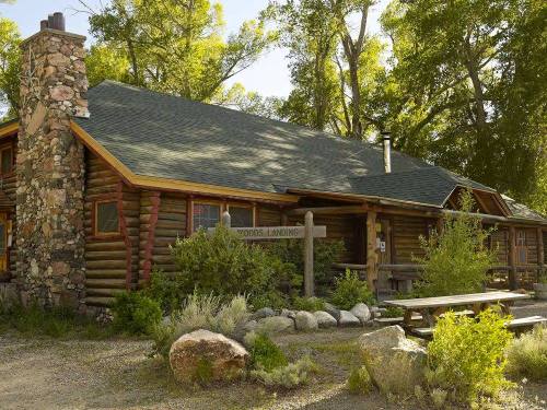 A rustic log cabin surrounded by trees, featuring a stone chimney and a picnic area with a wooden table.