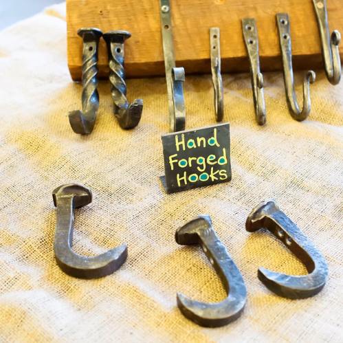 A display of hand-forged metal hooks on a wooden stand, with a sign reading "Hand Forged Hooks."