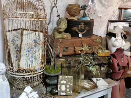 A vintage display featuring a birdcage, antique suitcases, a bust, and various decorative items on a table.