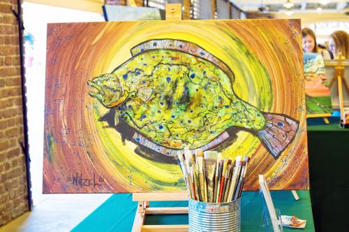 A colorful painting of a fish on an easel, with paintbrushes in a can in the foreground.
