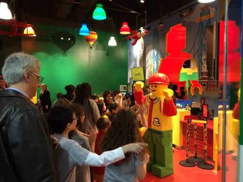 A colorful LEGO store with a large LEGO figure, children and adults interacting and exploring the vibrant displays.