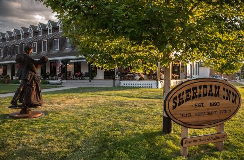 A historic inn with a sign reading "Sheridan Inn" and a statue of a couple dancing in a grassy area.