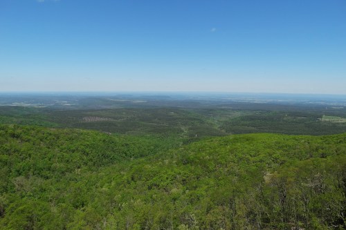 A panoramic view of lush green hills under a clear blue sky, stretching into the distance.