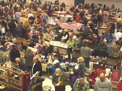 A bustling indoor market filled with people browsing various stalls and tables of goods.