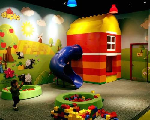 Colorful children's playroom with a slide, building blocks, and a large toy house against a bright mural.
