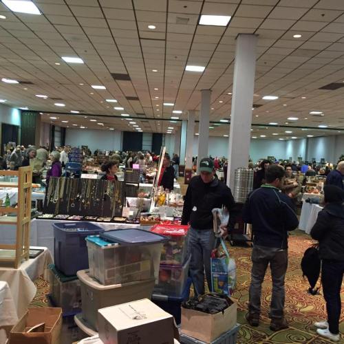 A bustling indoor market with numerous vendors and shoppers browsing various items in a large hall.