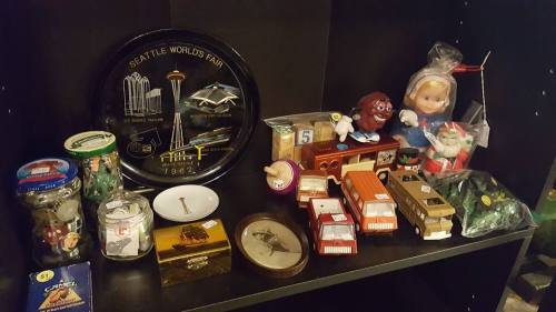A shelf displaying various collectibles, including a Seattle World's Fair plate, toys, and vintage items.