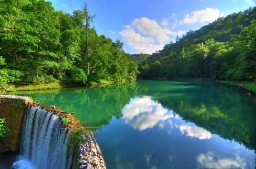 A serene landscape featuring a waterfall cascading into a calm, reflective lake surrounded by lush green trees.