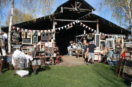 A rustic barn filled with vintage items, surrounded by greenery and decorated with colorful bunting.
