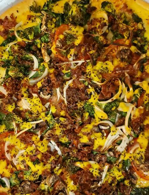 A close-up of a pizza topped with vegetables, herbs, and crispy bits, featuring vibrant colors and a golden crust.