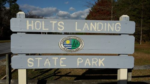 Sign for Holts Landing State Park, featuring the park's name and logo, set against a clear blue sky.