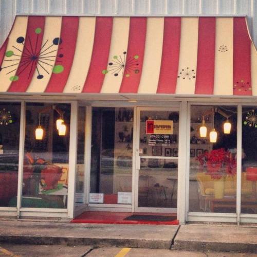 A storefront with a colorful striped awning and decorative elements, featuring a glass door and warm lighting inside.