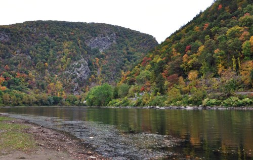 A serene river flows between colorful autumn hills, reflecting the vibrant foliage along the banks.