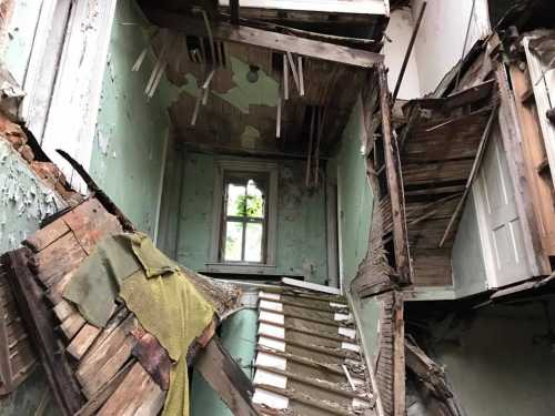 An abandoned room with crumbling walls, exposed wood, and a staircase leading to a window, showcasing decay and neglect.