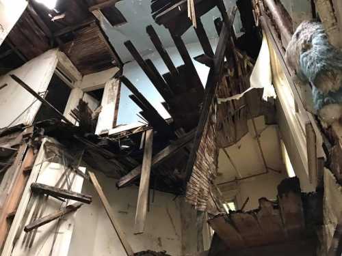 A damaged interior with a collapsed ceiling, exposing wooden beams and debris in a dilapidated building.