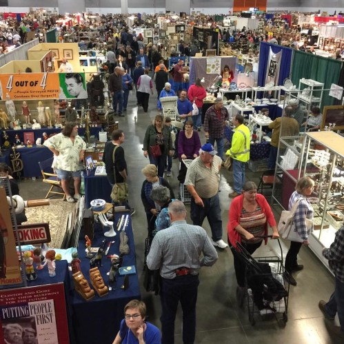 A crowded indoor market with numerous booths and people browsing various items for sale.