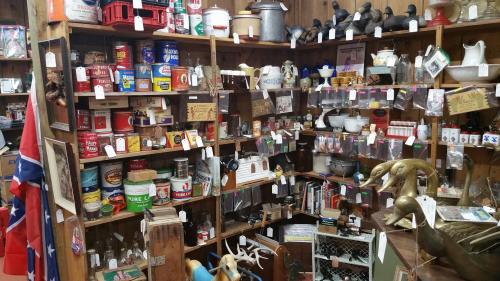 A cluttered antique shop display filled with various vintage items, jars, and collectibles on wooden shelves.