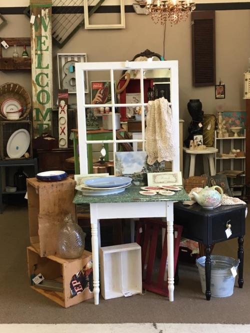 A vintage display featuring a white table, decorative items, and various antiques in a cozy shop setting.