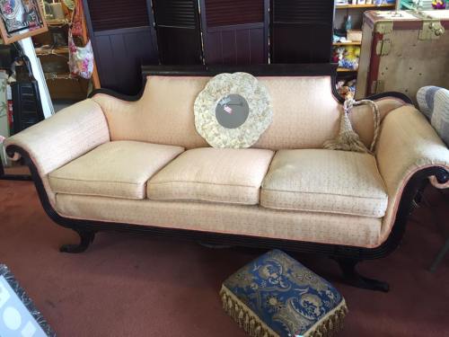 A vintage sofa with a light fabric, ornate wooden frame, and decorative pillow, set in a cozy shop environment.