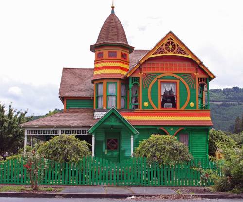 Colorful Victorian house with intricate details, a turret, and a green picket fence surrounded by trees.