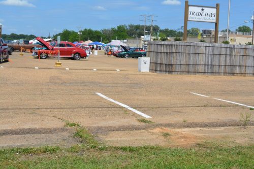 A parking lot with a sign for "Trade Days," featuring cars and tents in the background under a blue sky.