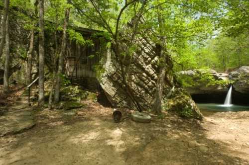 A rustic cabin nestled among trees, with a large rock formation and a small waterfall nearby.