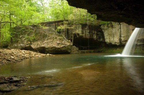 A serene scene of a waterfall cascading into a calm pool, surrounded by lush greenery and rocky cliffs.