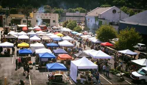 A bustling outdoor market with numerous colorful tents and a crowd of people shopping and socializing.