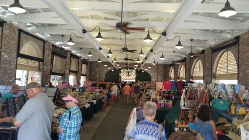A bustling indoor market with vendors selling various items, featuring shoppers browsing colorful displays.
