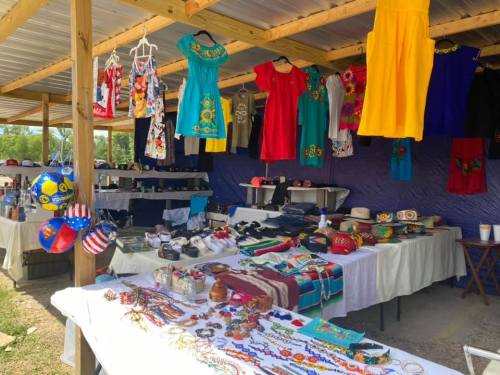 A vibrant market stall displaying colorful clothing, jewelry, and accessories under a shaded roof.